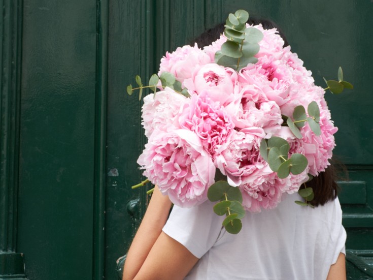 woman with a peony bouquet in front of a green door