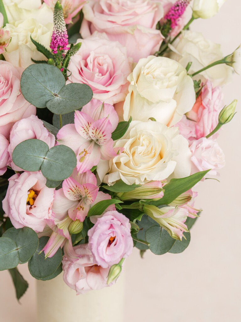 A bouquet of soft pink and ivory flowers in a tall white vase