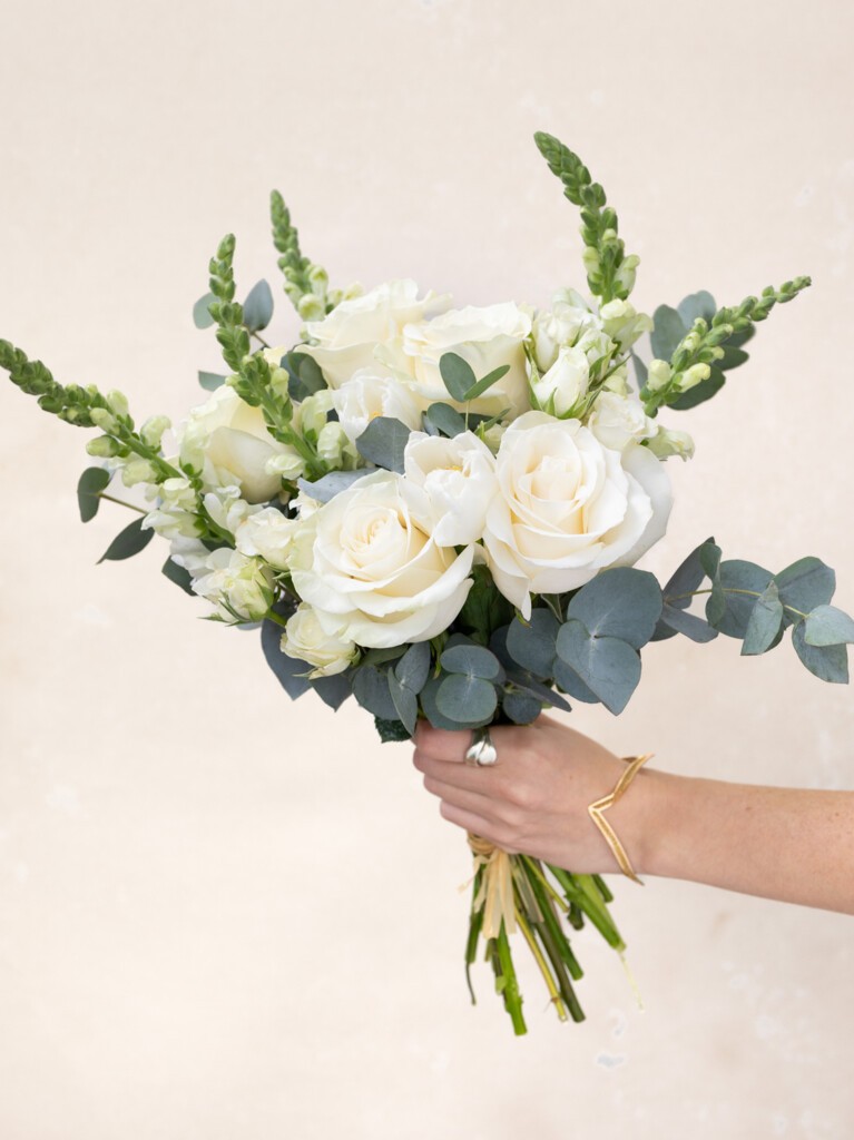 Handheld Paulette bouquet with 16 white stems including roses, snapdragons, and eucalyptus. Elegant, artisan-crafted gift for weddings or baby showers.