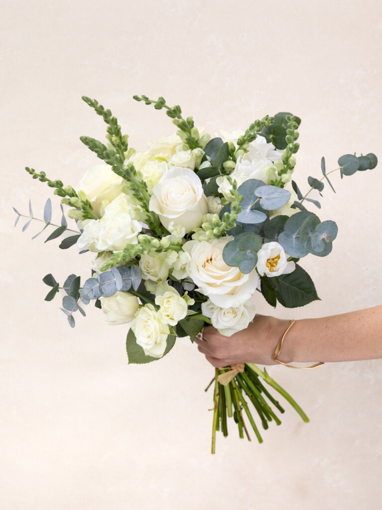 Handheld Paulette bouquet with 26 white blooms, showcasing roses, tulips, and eucalyptus. A luxurious floral gesture for meaningful milestones or modern weddings.