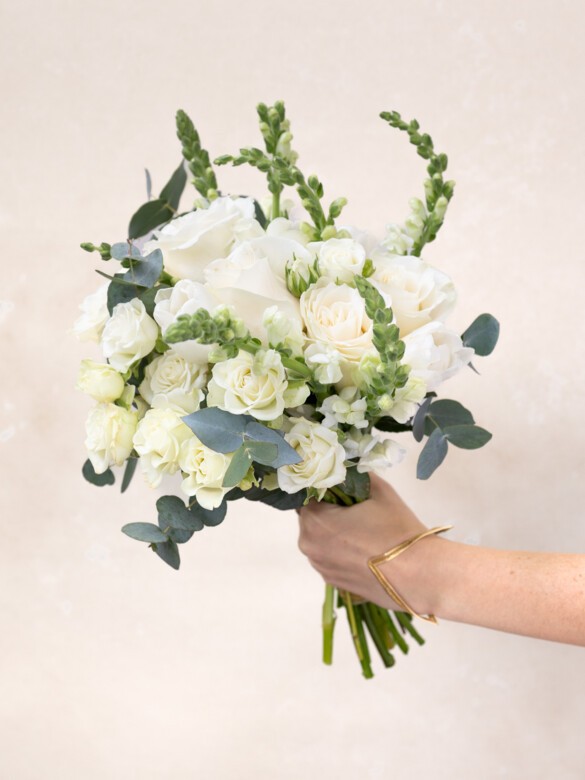 Handheld Paulette bouquet with 21 white flowers, including roses, snapdragons, and eucalyptus. Elegant gift for weddings, housewarmings, or just-because gestures.