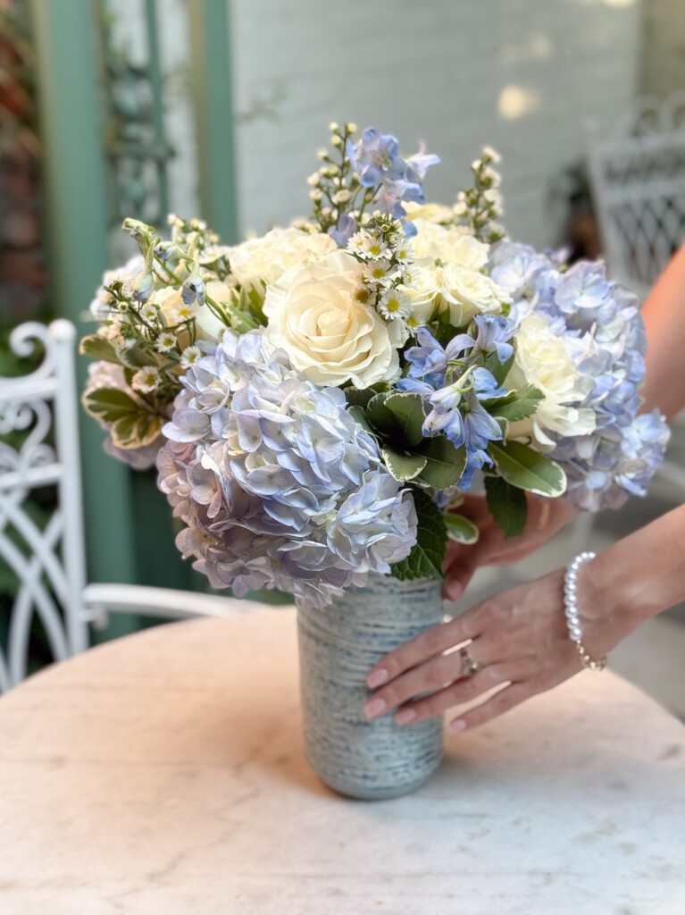 Enora bouquet being set in in blue ceramic vase on a garden table